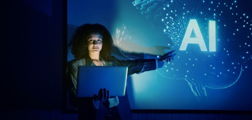 A person holding a laptop and gesturing toward a screen displaying the letters “AI” with a glowing digital brain graphic in the background.