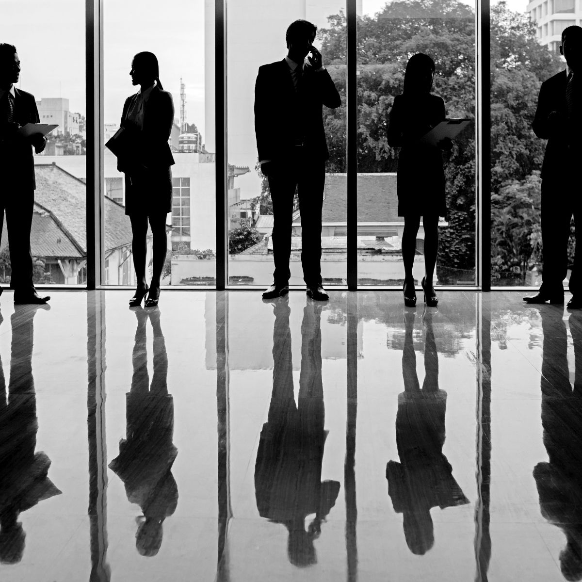 Silhouettes of business professionals standing in front of large windows with reflections on a polished floor.