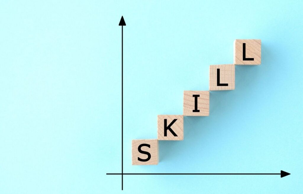 Wooden blocks arranged in an upward staircase spelling “SKILL” beside an upward graph, representing growth, progress, and increasing capability.