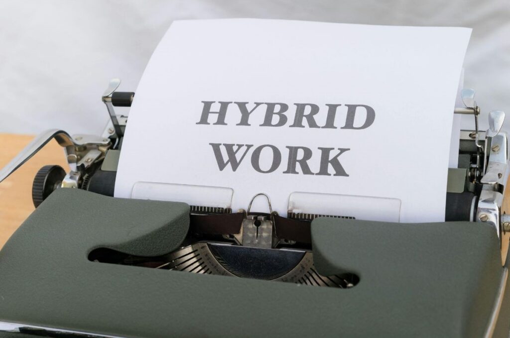 A sheet of paper in a typewriter with the words “HYBRID WORK” typed on it, representing a mix of in-office and remote work arrangements.