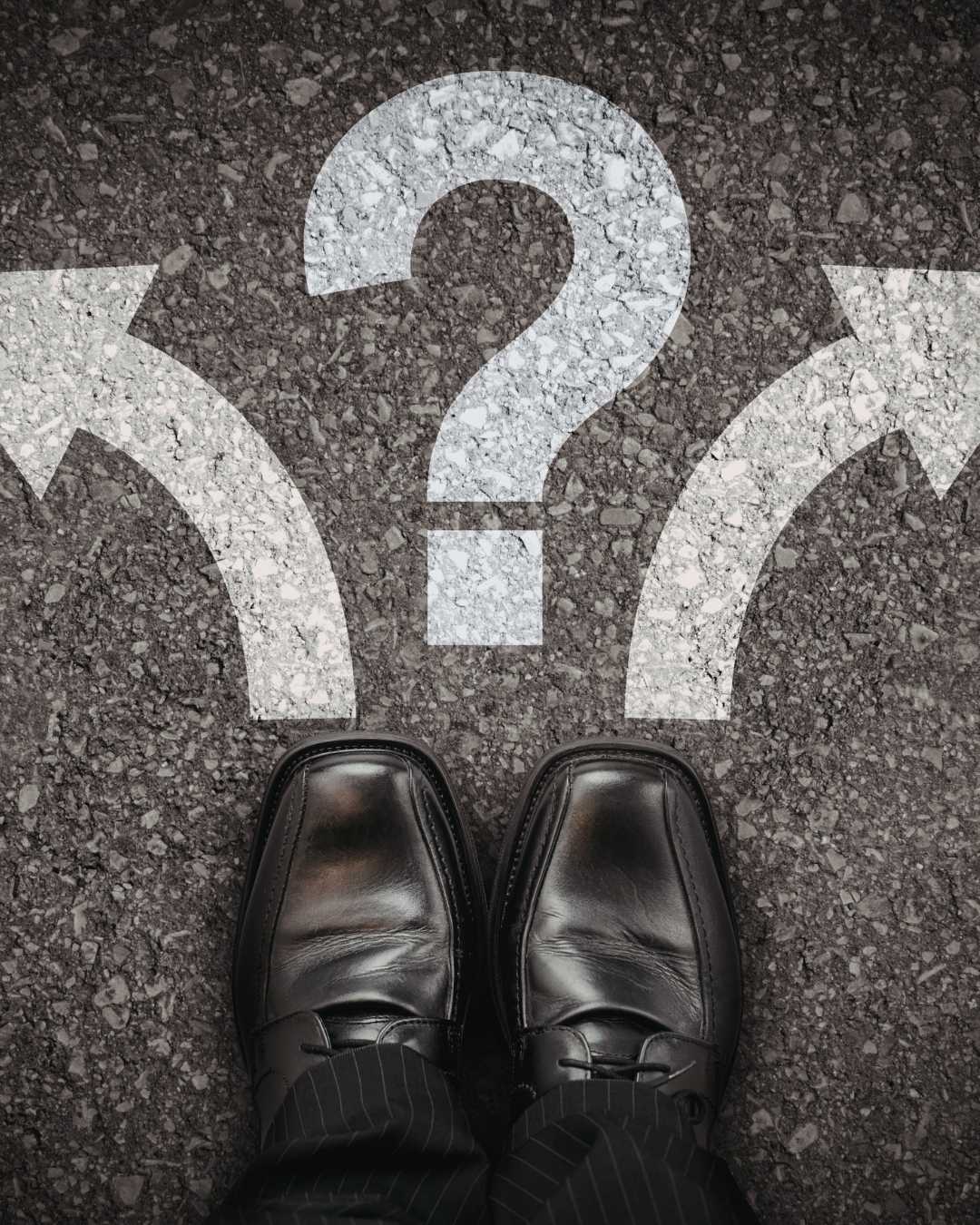 A person standing at a fork in the road with directional arrows and a large question mark, representing decision-making under uncertainty and the challenge of choosing between multiple