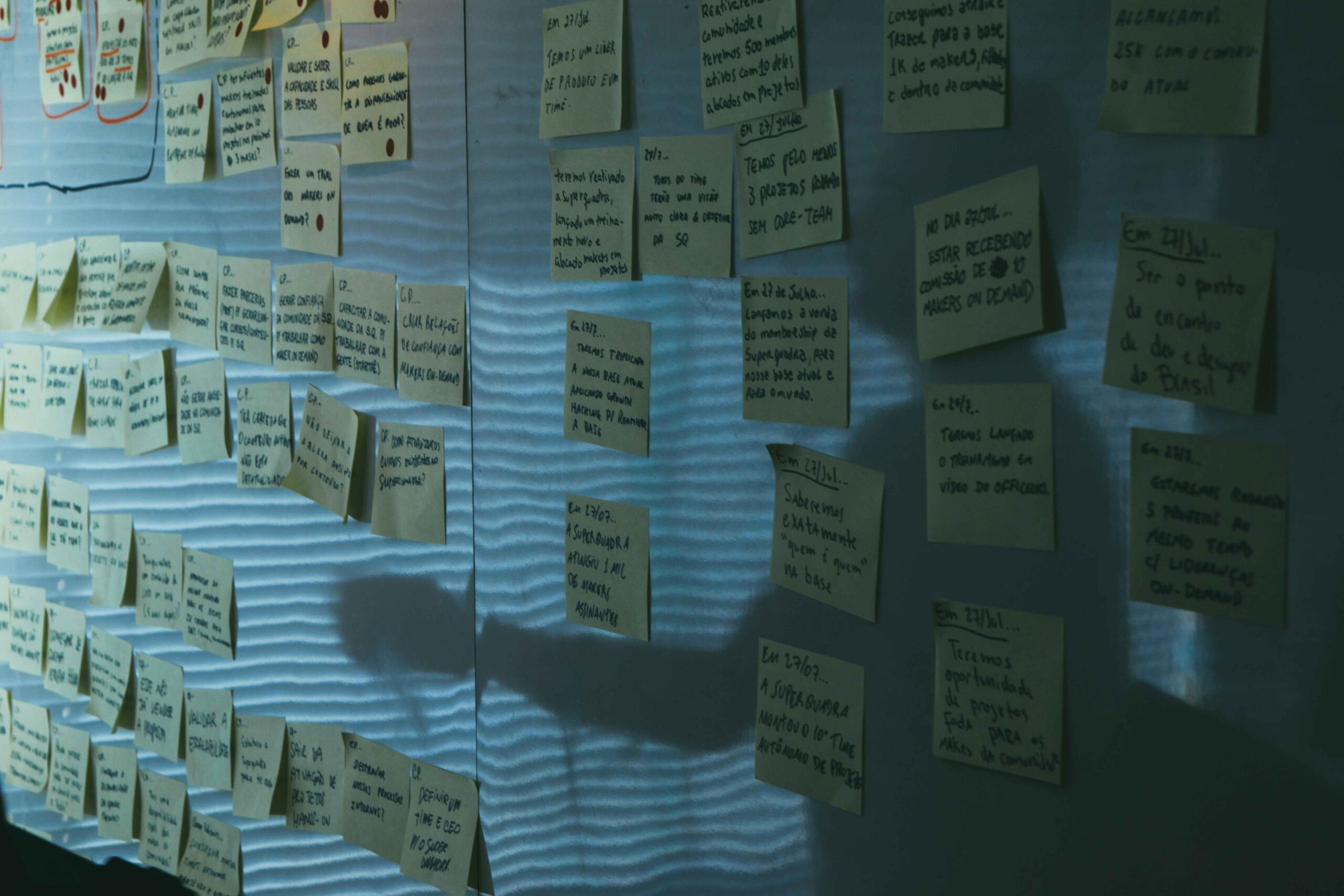 Conceptual illustration of a wall covered in handwritten sticky notes arranged in clusters, with a person’s shadow cast across them, suggesting planning, decision-making, or the accumulation of fragmented ideas and tasks.